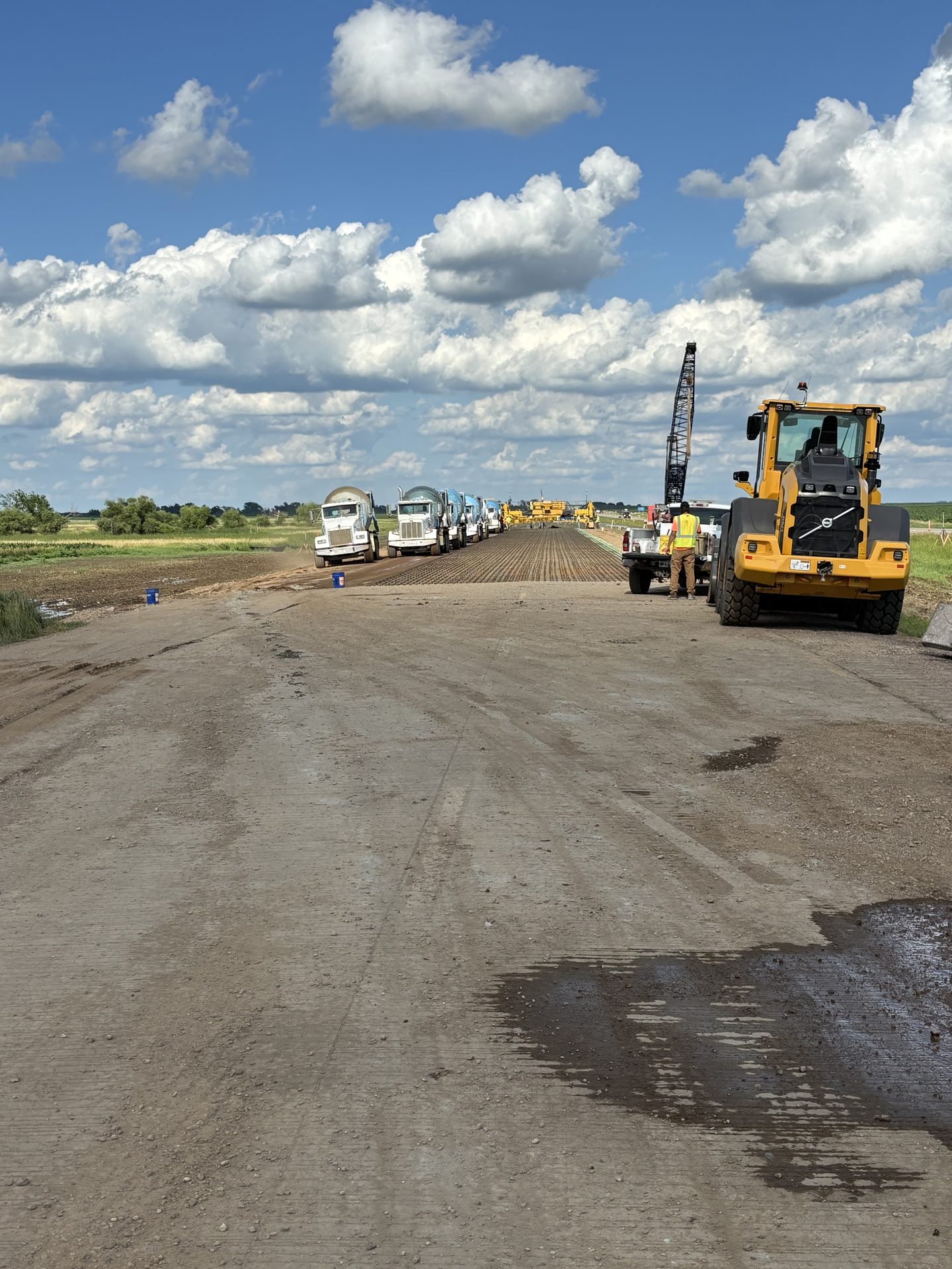 A line of mixer trucks on a rural road paving project